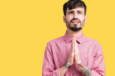 Yalvarıyor ve umut ifade yüzünde çok duygusal ve endişe ile birlikte elleriyle dua izole arka plan üzerinde pembe gömlek giymiş yakışıklı delikanlı. Bağışlanmak. Din kavramı.