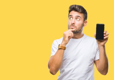 Yakışıklı delikanlı gösteren smartphone ekran izole arka plan ciddi bir yüz düşünme hakkında soru, çok karışık bir fikir üzerinde