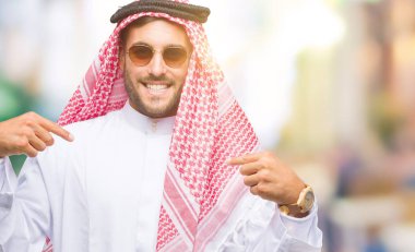 Yüzünde gülümseme ile kendinden emin görünüyorsun, kendini gururlu ve mutlu parmakları ile işaret izole arka plan üzerinde keffiyeh giyen genç yakışıklı adam.