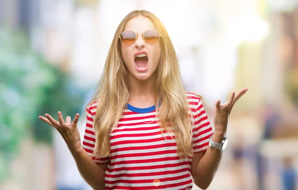 Genç güzel sarışın kadın üzerinde güneş gözlüğü takıyor arka plan deli izole ve deli bağırarak ve agresif ifade ve silah kaldırdı bağırıyor. Hayal kırıklığı kavramı.