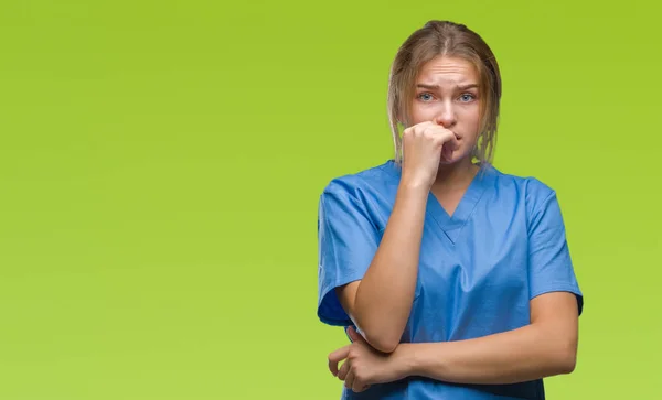 不安や両手の爪を噛んで口の中で緊張を探して孤立の背景の上の外科医の制服を着て若い白人の看護師の女性 不安の問題 — ストック写真