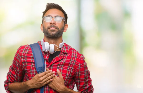 Adult hispanic student man wearing headphones and backpack over isolated background smiling with hands on chest with closed eyes and grateful gesture on face. Health concept.