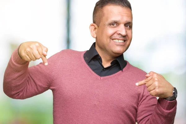 Middle age arab man over isolated background looking confident with smile on face, pointing oneself with fingers proud and happy.