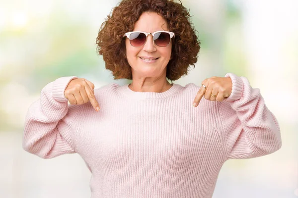 美しい中間エイガー年配の女性の顔に笑顔と自信を持って 誇りと幸せな指で自分を指している孤立した背景にピンクのセーター サングラスを着て — ストック写真