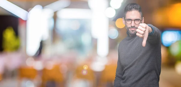 Young handsome man wearing glasses over isolated background looking unhappy and angry showing rejection and negative with thumbs down gesture. Bad expression.