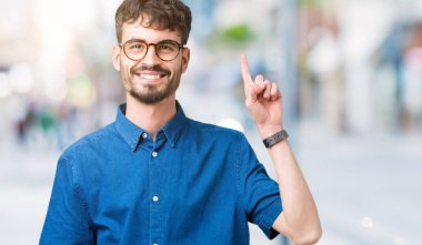 Ve kendinden emin ve mutlu gülümseyerek süre parmak numaralı yukarıyı gösteren izole arka plan üzerinde gözlük takan genç yakışıklı adam.