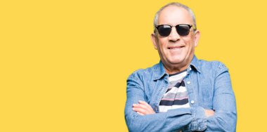 Denim ceket ve güneş gözlüğü mutlu yüz çapraz silah kameraya bakarak ile gülümseyen giymiş yakışıklı komuta sizde. Olumlu bir kişi.