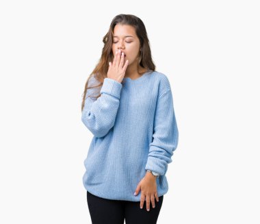 İzole arka plan üzerinde mavi kış kazak giyen genç güzel esmer kadın esneme yorgun kapsayan ağız el ile sıkılmış. Restless ve uyku hali.