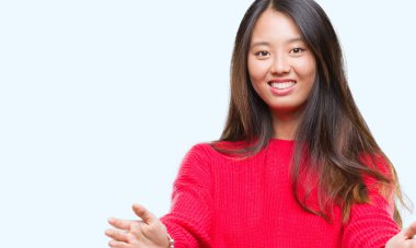 Sarılmak için kollarını açarak gülümseyerek kameraya bakarak izole arka plan üzerinde kış kazak giyen genç Asyalı kadın. Neşeli ifade kucaklayan mutluluk.