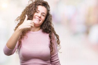 Güzel esmer kıvırcık saçlı Genç kız mutlu yaşasın el ile jest yapıyor izole arka plan üzerinde pembe kazak giyiyor. Kameraya bakarak başarı gösteren ile ifade onaylama.