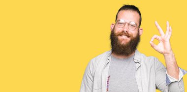 El ve parmak ile ok işareti yapıyor olumlu gülümseyen gözlüklü genç sarışın adam. Başarılı ifade.