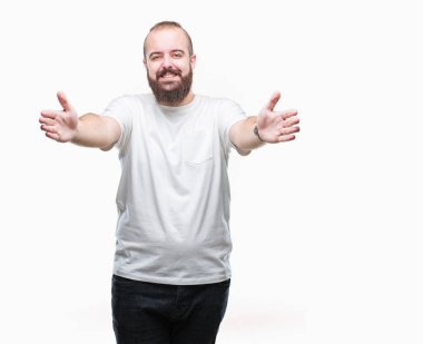 Sarılmak için kollarını açarak gülümseyerek kameraya bakarak izole arka plan üzerinde rahat t-shirt giyen genç beyaz hipster adam. Neşeli ifade kucaklayan mutluluk.