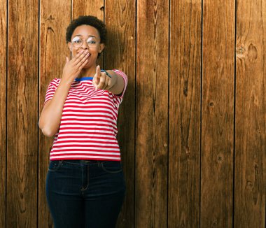 Güzel genç Afro-Amerikan kadın gözlük izole üzerinde gülme sizin parmak el kamerasıyla ağzına, utanç ifadesi işaret eden arka plan