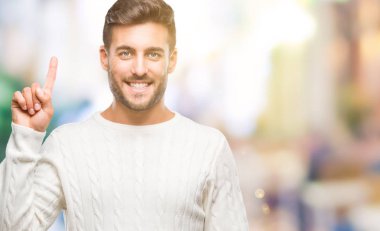 Ve parmak gülümseyen süre bir numara ile kendinden emin ve mutlu yukarıyı gösteren izole arka plan üzerinde kış kazak giyen genç yakışıklı adam.