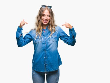 Yüzünde gülümseme ile kendinden emin görünüyorsun, kendini gururlu ve mutlu parmakları ile işaret izole arka plan üzerinde güneş gözlüğü takıyor güzel sarışın genç kadın.