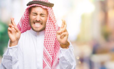 Umut ve gözleri kapalı geçiş parmaklarıyla gülümseyen izole arka plan üzerinde keffiyeh giyen genç yakışıklı adam. Şans ve batıl kavramı.