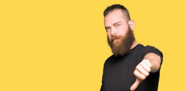 Mutsuz ve kızgın ret gösterilen ve başparmak aşağı hareketi ile negatif seyir rahat t-shirt giyen genç sarışın adam. Kötü ifade.