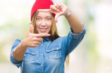 Elle yapma çerçeve ve parmakları ile mutlu yüz gülümseyen izole arka plan üzerinde yün kap giyen genç beyaz güzel kadın. Yaratıcılık ve Fotoğrafçılık kavramı.