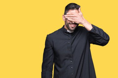 Genç Hıristiyan rahip gülümsüyor ve gözleri için sürpriz kapsayan yüz el ile gülüyor izole arka plan üzerinde. Kör kavramı.