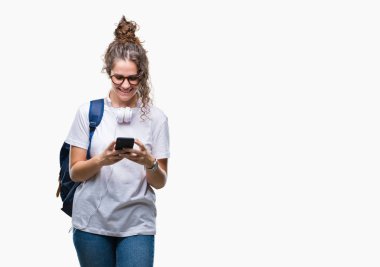 Sırt çantası, kulaklık ve smartphone izole arka plan üzerinde duran ve diş gösterilen kendine güvenen bir gülümsemeyle gülümseyerek mutlu bir yüz ile giyen genç esmer öğrenci kız