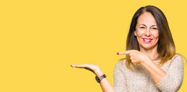 Hayret ve el ile sunulması ve parmak ile işaret ederken kameraya gülümseyen moda kazak giyen güzel orta yaş kadın.