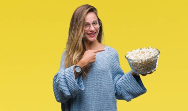 Genç güzel sarışın kadın izole arka el ve parmak ile işaret çok mutlu üzerinde patlamış mısır yemek