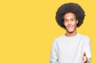 Afrikalı-Amerikalı genç afro saçlı tebrik ve konuksever dost sunan karşılıklı gülümseyen sportif kazak giyiyor. Başarılı iş.