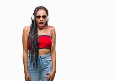 Korkuyor ve şok sürpriz ifade, korku ve heyecan yüz ile izole arka plan üzerinde kulaklık giyen Doğum işareti ile saç Afrikalı-Amerikalı genç örgülü.