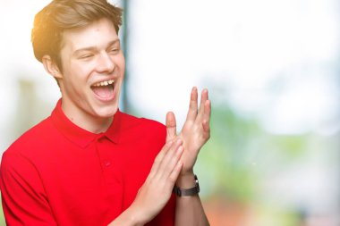 Genç yakışıklı adam giyen kırmızı t-shirt üzerine izole arka plan Clapping ve mutlu ve neşeli, gururlu gülümseyen birlikte eller alkış