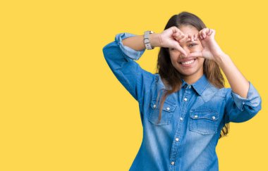 İzole arka plan yaparken kalp şekli el ve parmak işareti seyir gülümseyen ile üzerinde mavi kot gömlek giyen genç güzel esmer kadın