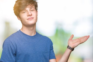 Neşeli sunulması ve kameraya bakarak avucunun ile işaret gülümseyen izole arka plan üzerinde mavi t-shirt giyen genç yakışıklı adam.