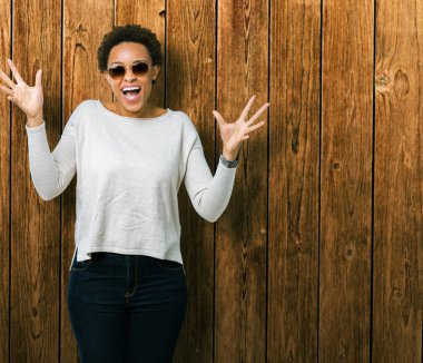 Güzel genç Afro-Amerikan kadın üzerinde güneş gözlüğü takıyor deli kutluyor arka plan izole ve silah ile başarı için yükseltilmiş ve açık gözleri heyecanlı çığlık hayrete düşürdü. Kazanan kavramı