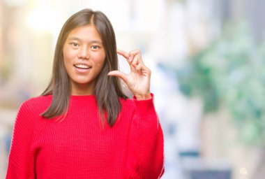 Asyalı genç gülümseyen izole arka plan ve boyutu işaret parmaklı ararken ve kamera işi el ile kendinden emin eller üzerinde kış kazak giyiyor. Ölçü kavramı.