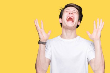 Yakışıklı delikanlı deli ve silah ile başarı için deli kutluyor izole arka plan üzerinde rahat beyaz t-shirt giyen kaldırdı ve heyecanlı çığlık gözler kapalı. Kazanan kavramı