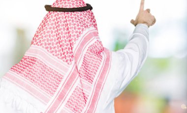 Arap iş adamı geleneksel keffiyeh giymiş uzun saçlı eşarp geriye doğru arkasında parmak eliyle işaret Posing