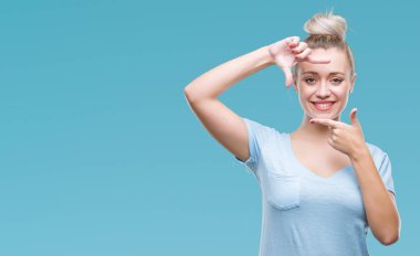 Genç Sarışın kadın elle yapma çerçeve ve parmakları ile mutlu yüz gülümseyen izole arka plan yüzünden. Yaratıcılık ve Fotoğrafçılık kavramı.