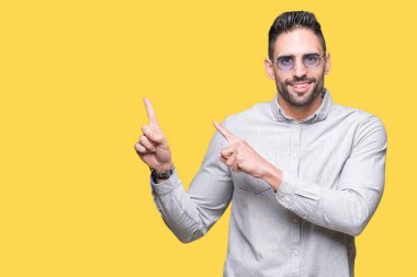 Yakışıklı delikanlı gülümseyen ve iki elleri ve parmakları ile tarafına işaret kamera bakarak izole arka plan üzerinde güneş gözlüğü takıyor.