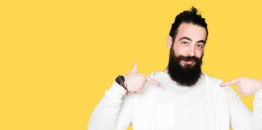 Uzun saç ve sakal yüzünde gülümseme ile kendinden emin görünüyorsun, kendini gururlu ve mutlu parmakları ile işaret sportif sweatshirt giyen genç adamla.