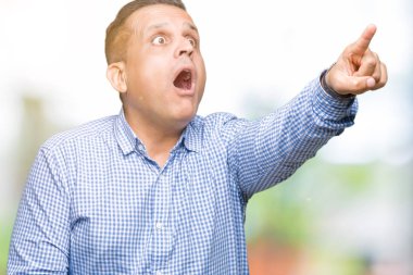 Orta yaş Arap iş adamı izole arka plan ile sürpriz devam et, parmakla üzerinde açık ağız ifade, önünde bir şey hayret