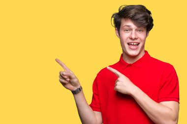 Gülümseyen ve iki elleri ve parmakları ile tarafına işaret kamera bakarak izole arka plan üzerinde kırmızı t-shirt giyen genç yakışıklı adam.