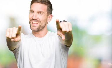 Olumlu ve neşeli gülümseyen casual beyaz t-shirt işaretleme ve parmaklar, kamerayla giyen yakışıklı adam