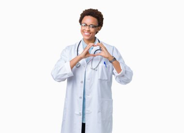 Genç Afro-Amerikan doktor kadın kalp simgesi ve elleriyle şekil gösterilen aşık gülümseyen izole arka plan üzerinde tıbbi bir palto giyiyor. Romantik kavramı.