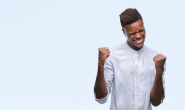 Gülümseyen ve başarı için çığlık genç Afro-Amerikan adam izole arka plan çok mutlu ve heyecanlı kaldırdı, silah ile kazanan jest yapıyor. Kutlama kavramı.