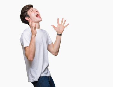 Üzerinde rahat beyaz t-shirt giyen genç yakışıklı adam deli kutluyor arka plan izole ve başarı için kaldırdı kollarını açarak hayrete ve heyecanlı çığlık gözleri açık. Kazanan kavramı