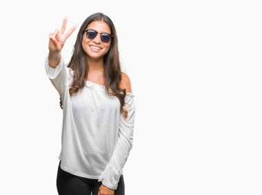 Genç güzel Arap kadın mutlu yüz zafer işareti yaparken kameraya göz kırpıyor ile gülümseyen izole arka plan üzerinde güneş gözlüğü takıyor. İki numaralı.