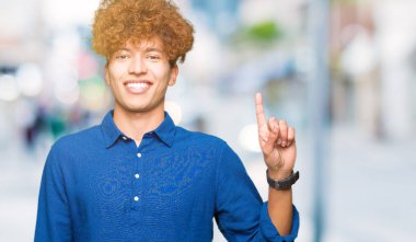 Gösterilen ve kendinden emin ve mutlu gülümseyen bir parmak ile işaret eden oktan yukarı afro saçlı Genç yakışıklı zarif adam.