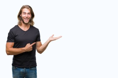 Hayret ve el ile sunulması ve parmak ile işaret ederken kameraya gülümseyen izole arka plan üzerinde uzun saçlı yakışıklı delikanlı.