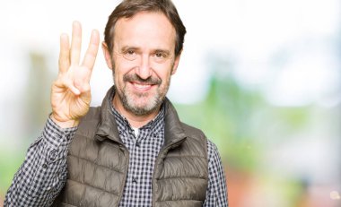 Kış yelek gösterme ve parmakları ile işaret giyen orta yaş yakışıklı adam kendinden emin ve mutlu gülümseyerek iken üçüncü.