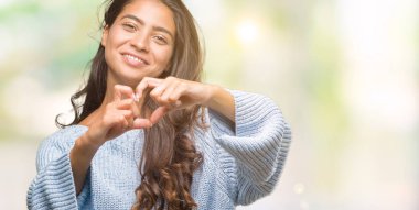 Kalp simgesi ve elleriyle şekil gösterilen aşık gülümseyen izole arka plan üzerinde kış kazak giyen genç güzel Arap kadın. Romantik kavramı.