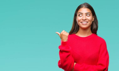 Seyir ve başparmak yanında yukarıyı mutlu yüz ile gülümseyen izole arka plan üzerinde kış kazak giyen genç güzel Arap kadın.